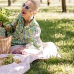 Elderly woman enjoying a picnic with vibrant clothing and fresh greenery.