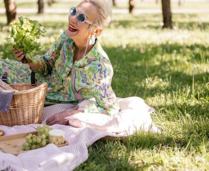 Elderly woman enjoying a picnic with vibrant clothing and fresh greenery.