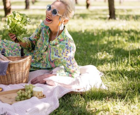 Elderly woman enjoying a picnic with vibrant clothing and fresh greenery.
